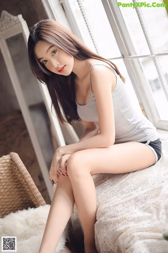 A woman sitting on top of a bed next to a window.