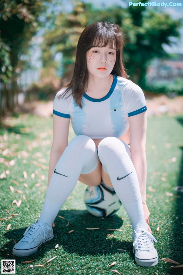 A woman sitting on the ground with a soccer ball.
