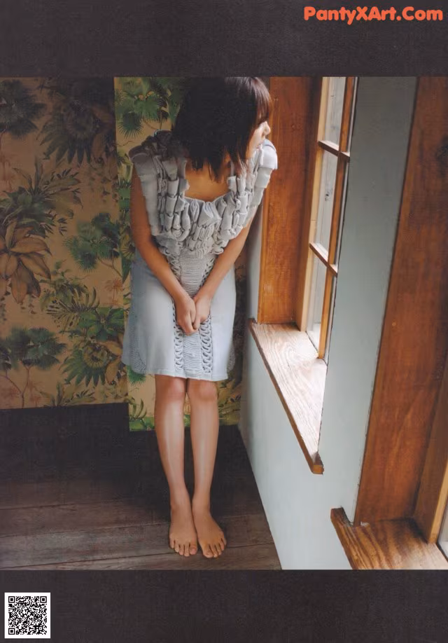 A woman standing in front of a window looking out the window.