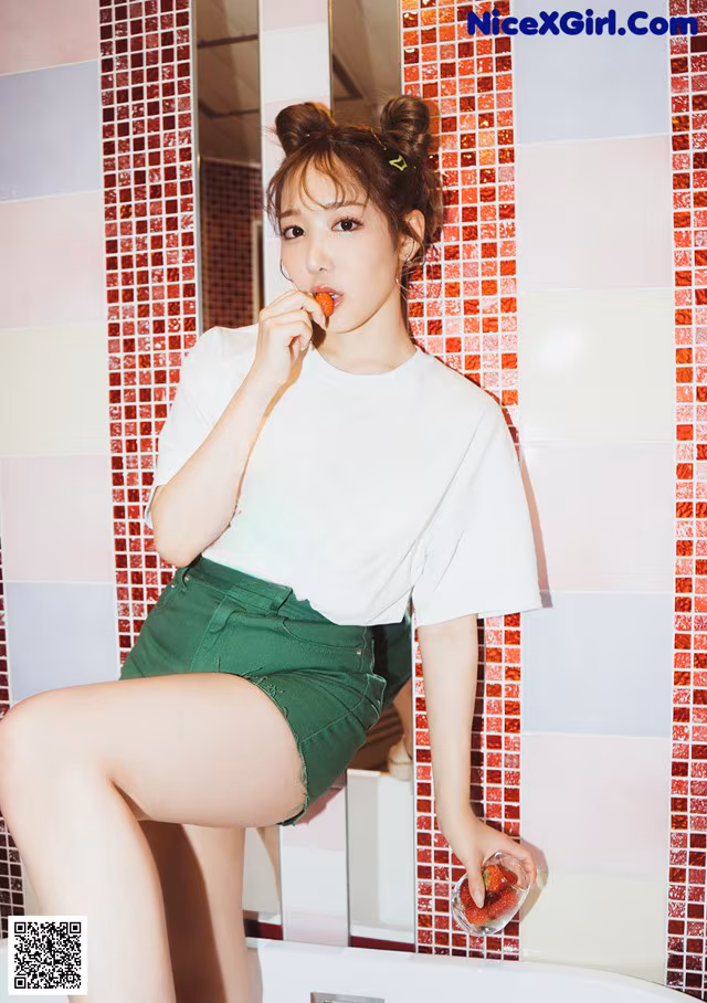 A woman sitting in a bathtub eating a strawberry.