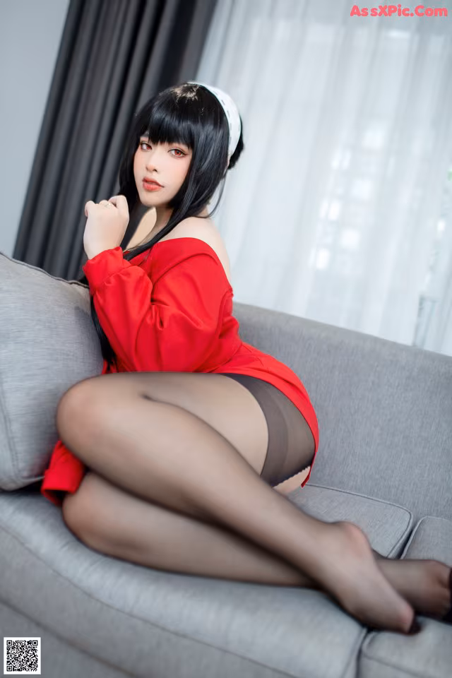 A woman in a red dress sitting on a gray couch.
