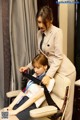 A woman in a suit and tie sitting on a chair next to a young girl.