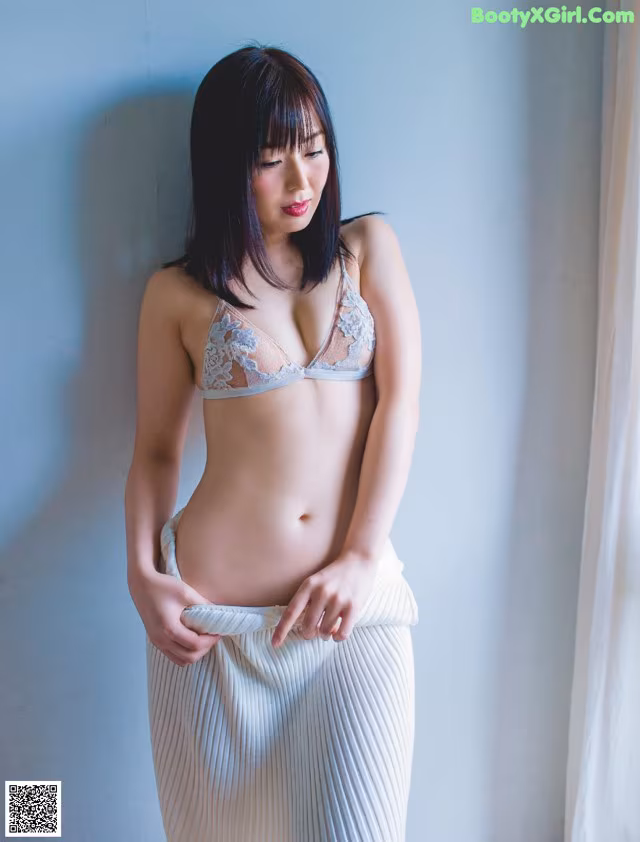 A woman in a white bra and skirt leaning against a wall.
