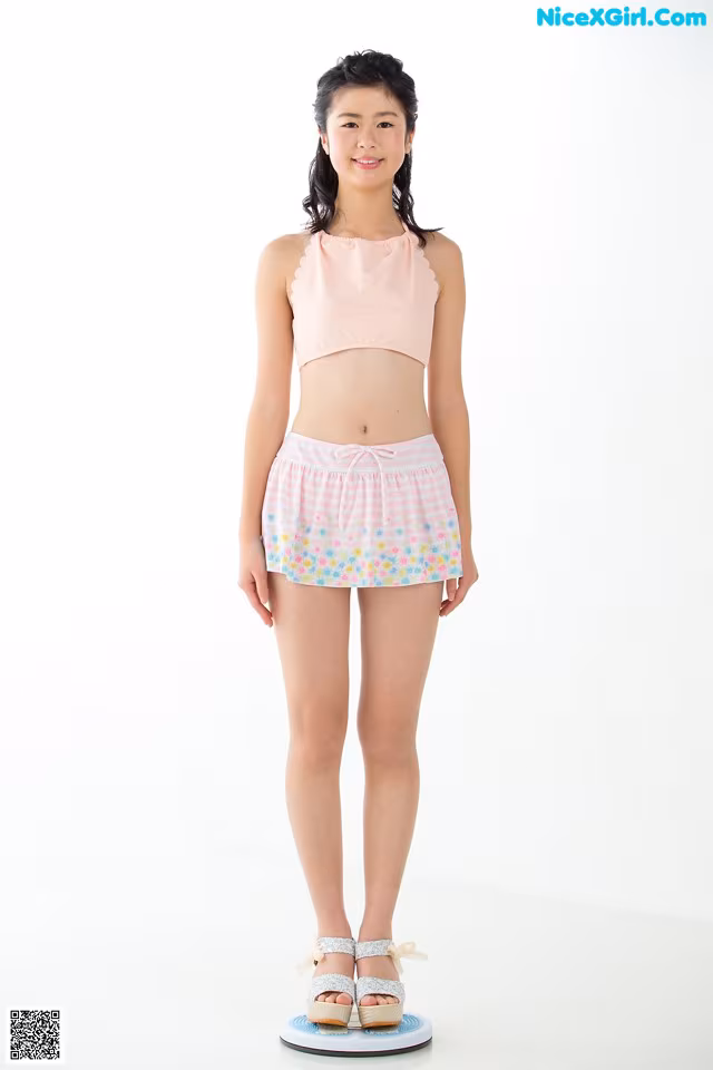 A young woman standing on a scale wearing a pink top and shorts.