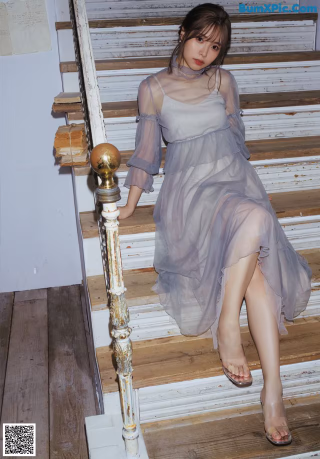 A woman in a gray dress sitting on a set of stairs.