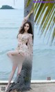 A woman leaning against a palm tree on the beach.