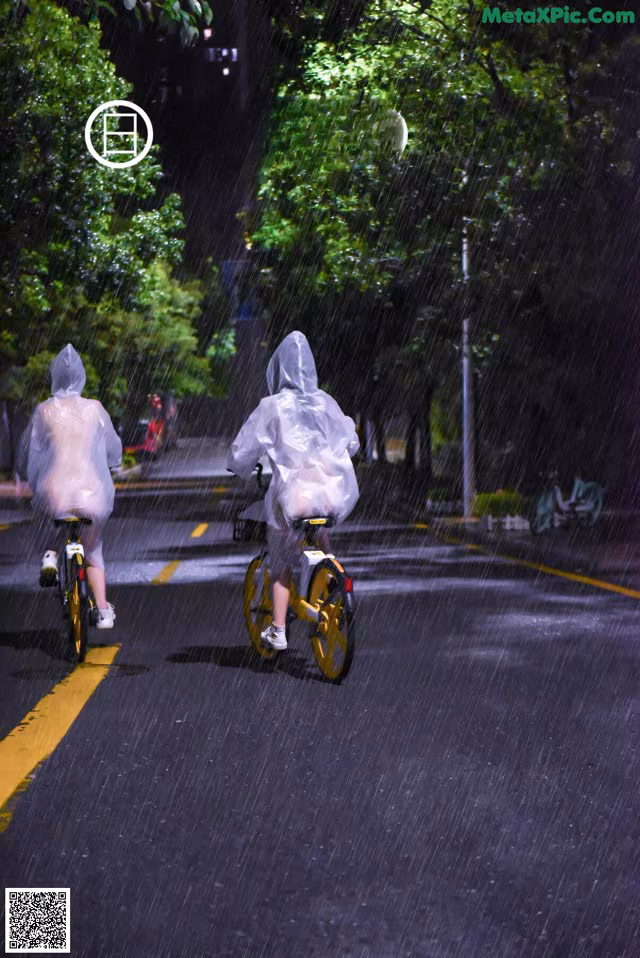 A couple of people riding bikes down a street in the rain.