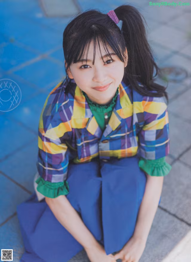 A young woman sitting on the ground wearing a colorful shirt and skirt.